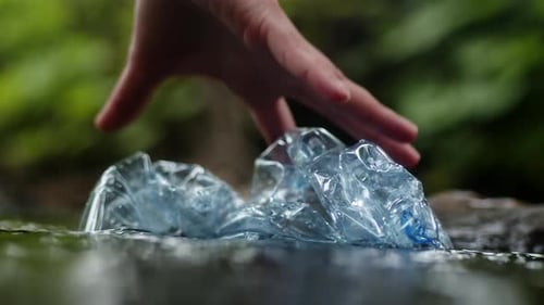 A Man's Hand Cleans a Pond of Plastic Bottles Close Up