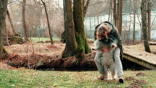 a man holds his dog on his belly and strokes it. You are in a small forest in autumnal background. T