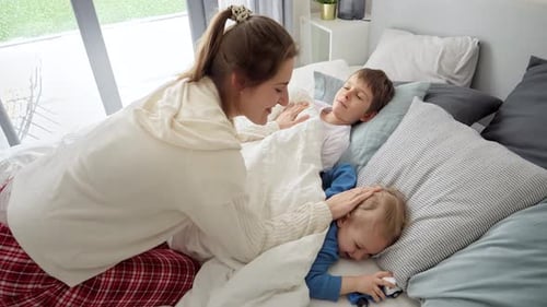Mother Tucking Children into Bed at Home