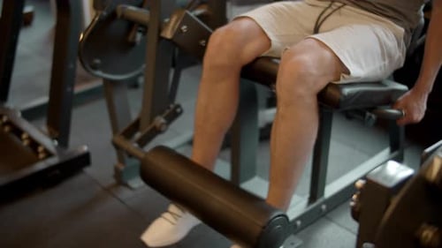 Closeup Homem forte com pernas treinando na academia. Homem de fisiculturismo irreconhecível fazendo
extensões de pernas...