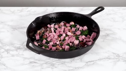 Filling in Cast Iron Skillet with Vegetables to Prepare Spinach and Ham Frittata