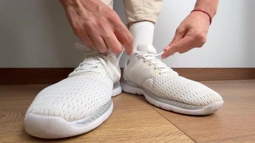 Close Up of a Woman Tying Shoelaces on White Sneakers Indoors Sport Shoes on Wooden Floor Preparing