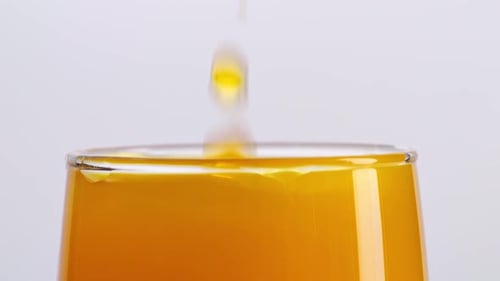 Close Up Of Ice Cube Falling In A Glass Of Orange Juice On The Light White Screen Background