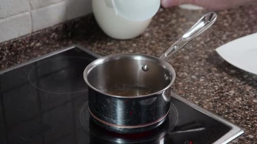 Pouring Water From Glass Jar Into Steel Pot on Induction Stove Cooking Preparation