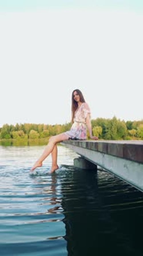 Joyful Woman Splashing Her Feet In Water Sitting On Pier