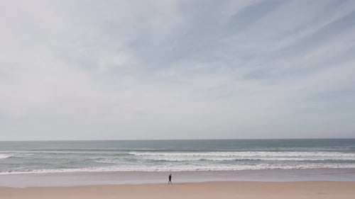 Solitary Man Walking on Sandy Beach with Waves and Clear Sky