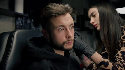 Tattoo piercing studio - a woman makes an ear piercing to a man to a guy