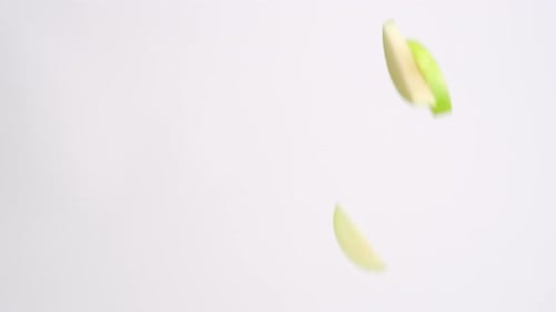 Green apple fruit slices falling through the air on white backdrop in slow motion