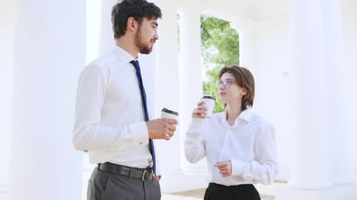 Geschäftspaar genießt an einem sonnigen Tag Kaffee im Freien an einem Ort mit weißen Säulen, während es sich verlobt