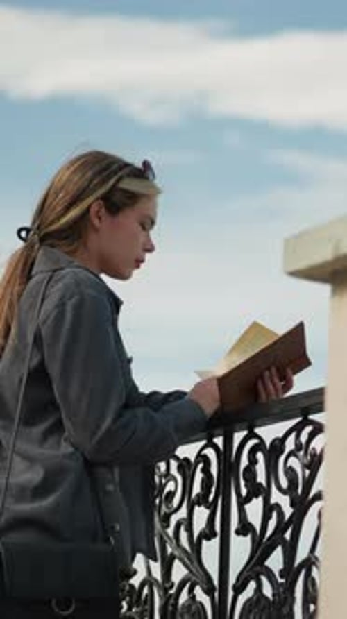 Young Woman Reading Book on City Balcony