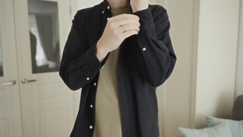 Young Man Buttons Shirt Cuffs in Bedroom