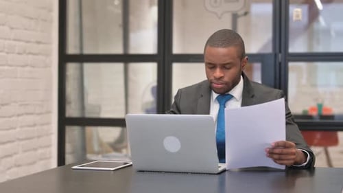 Man Looks at Paperwork in Office at Desk