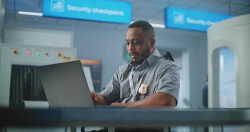Airport Security Checkpoint Security Officer Using Laptop Computer Looking at Camera