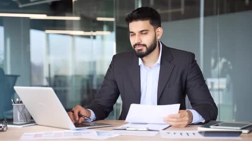 Portrait of serious male financier sitting at desk at workplace in modern business office.