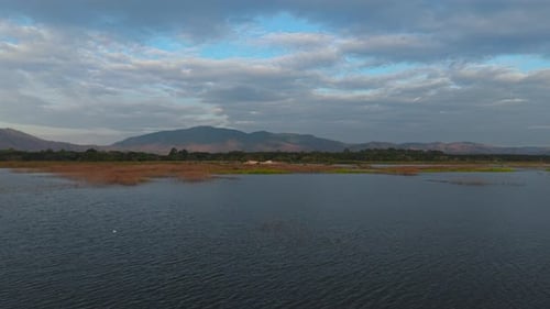 Wide Expanse of Calm Blue Water with Distant Wetlands Backed By Forested Hills and Mountains Under a