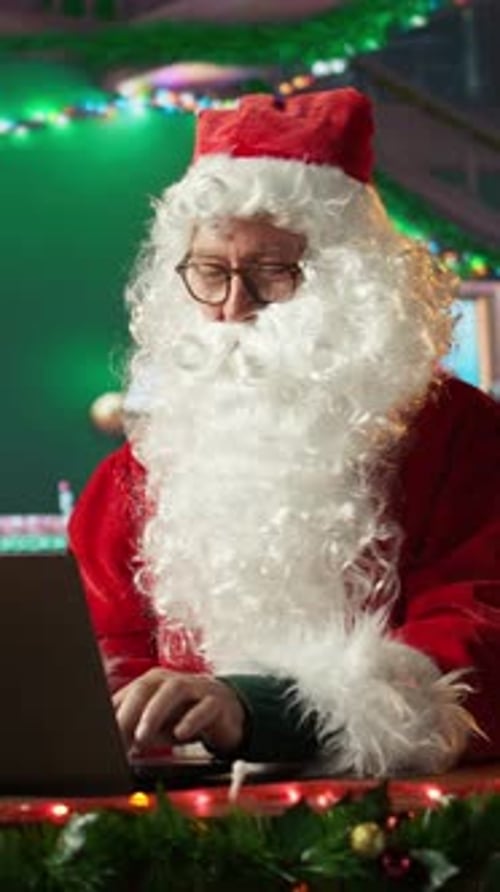 Vertical Video Father Christmas Browsing Websites on Laptop and Checking Holiday Gift Lists