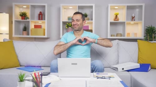 Home office worker man makes heart symbol looking at camera.
