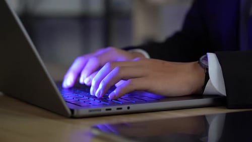 mãos masculinas digitando em um laptop à noite.