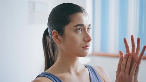 Young Woman Massaging Hands in Bright Room