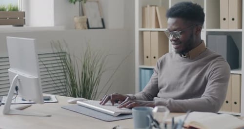 Cheerful African American Office Worker Using Computer Typing and Smiling Concentrated on Corporate