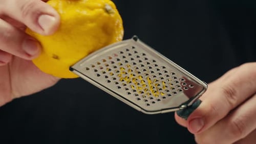 Makro-Nahaufnahme eines professionellen Kochs mit Zitrone und Reibe, bei dem Zitronenschale für Limonadensalat gerieben werden
