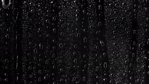 Close up rain on window, Water Drops following down on black background. Drops of Rain trickling dow