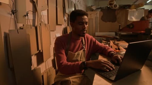Young African American Craftsman Using Laptop in Workshop