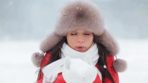 Woman in winter hat blowing snow to camera