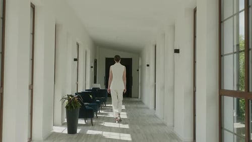 Stylish Model In White Trouser Suit Walks Through Hotel Lobby Back View