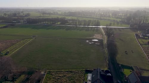 Aerial view of lush green pastures and rural farmland in Europe at sunrise. Misty horizon with wind