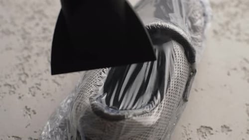 Closeup Top View of Unrecognizable Man Warming Up Shrink Wrap on Sneakers Inside for Careful Storage