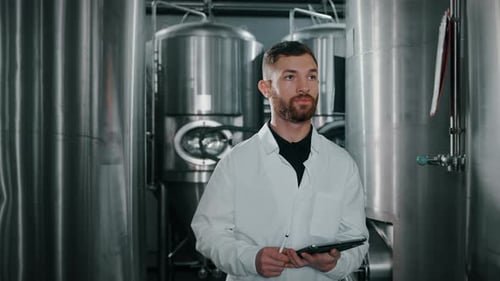 L'atelier d'un technologue moderne de la production d'aliments et de boissons marche entre des réservoirs cylindriques