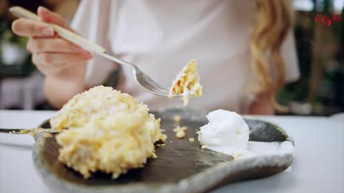 Close view of a woman eating a cake with ice cream with a fork in a cafe