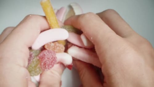 Top view, I take a handful of assorted and differently shaped mix of gummy candies in my hands.
