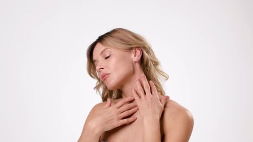 Woman With Light Skin Touching Her Neck and Posing Against a Plain Background