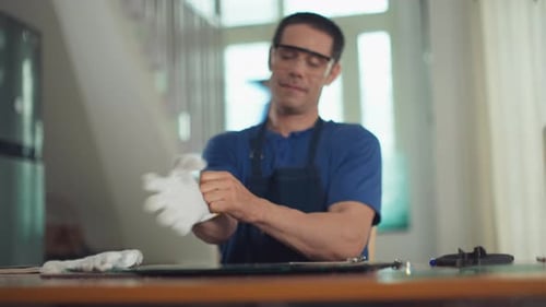 Craftsman Putting on Gloves Sitting at Working Desk at Glassware Studio