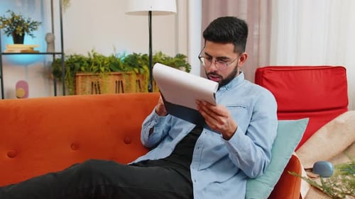 Young Adult Reviews Documents on an Orange Couch