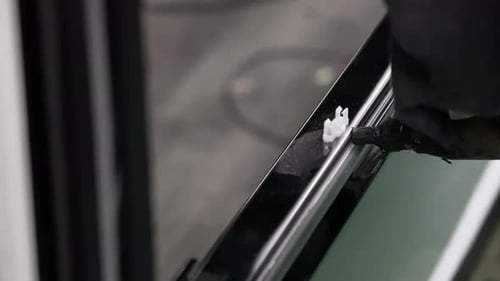 Technicien appliquant un scellant industriel noir sur le châssis d'une fenêtre de véhicule sur une chaîne de montage