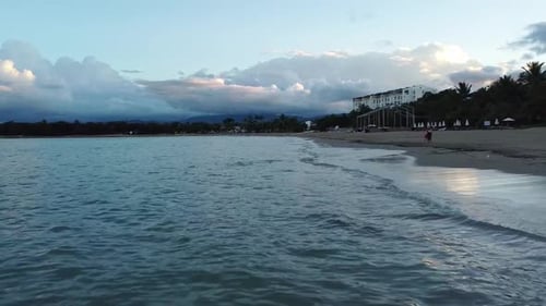 Low-flying drone shot over ocean waves at sunset along a tropical beach