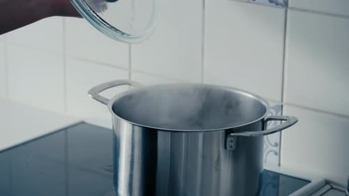 Close up of woman's hand opening the Lid on a big Iron Pot with boiling and steaming Water bubbling