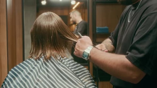 Skillful Young Barber Tapering Clients Hair while Working on Haircut