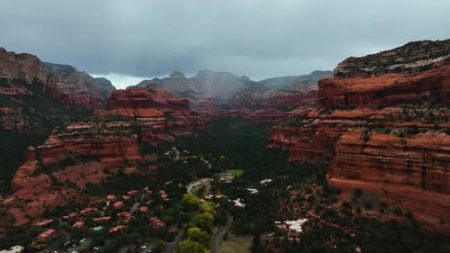 Sedona Town Surrounded By Red Rock Cliffs Under Overcast Sky In Arizona, USA. Aerial Drone Shot