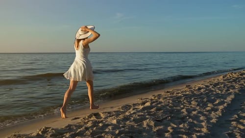 Verspielte Frau in schönem Kleid läuft am Strand bei goldenem Sonnenuntergang in Zeitlupe