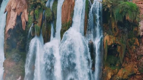 A Bird Flies in Front of a Stormy Waterfall on a Red Rock