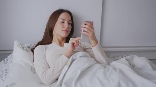 Woman Using Mobile Phone while Lying in Bed