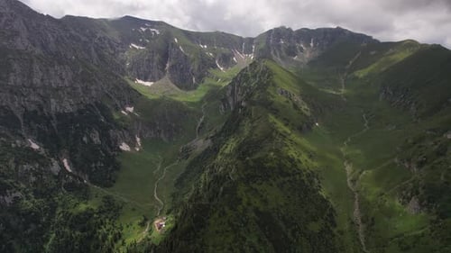 Lush Bucegi Mountains with green slopes under a cloudy sky, aerial shot