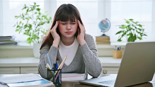 Sad Young Female College Student Sitting at Desk with Computer Experiencing Headache