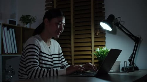 Woman working on laptop at night under lamp