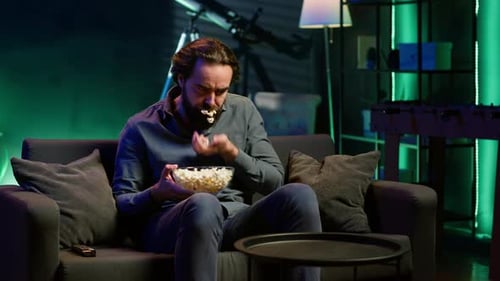 Un homme dans un appartement mangeant du pop-corn en regardant un film à la télévision