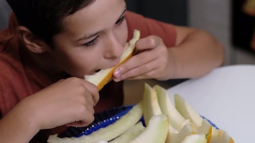 Un garçon déguste un morceau de melon en se concentrant intensément sur sa collation. La photo met l'accent sur le plaisir de